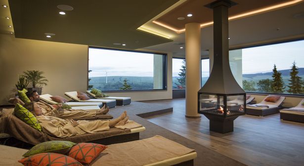 A man and a woman lying on a lounger at Elldus Resort Oberwiesenthal. Im Hintergrund kann man die Landschaft vom Erzgebirge sehen.